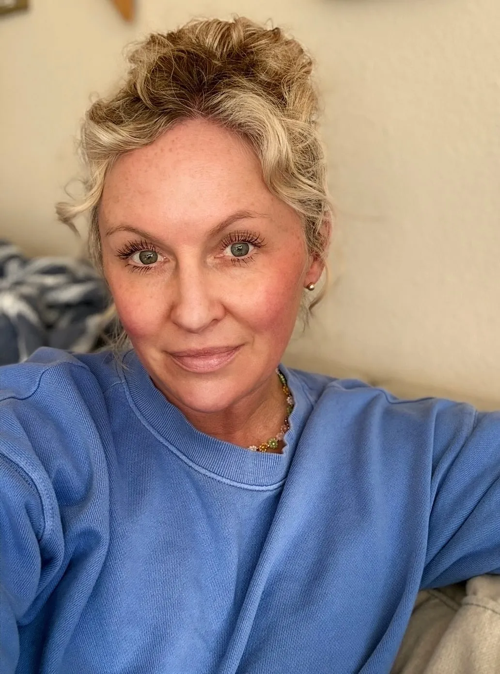Nicole smiling softly, her curly blonde hair pinned up, wearing a blue sweatshirt